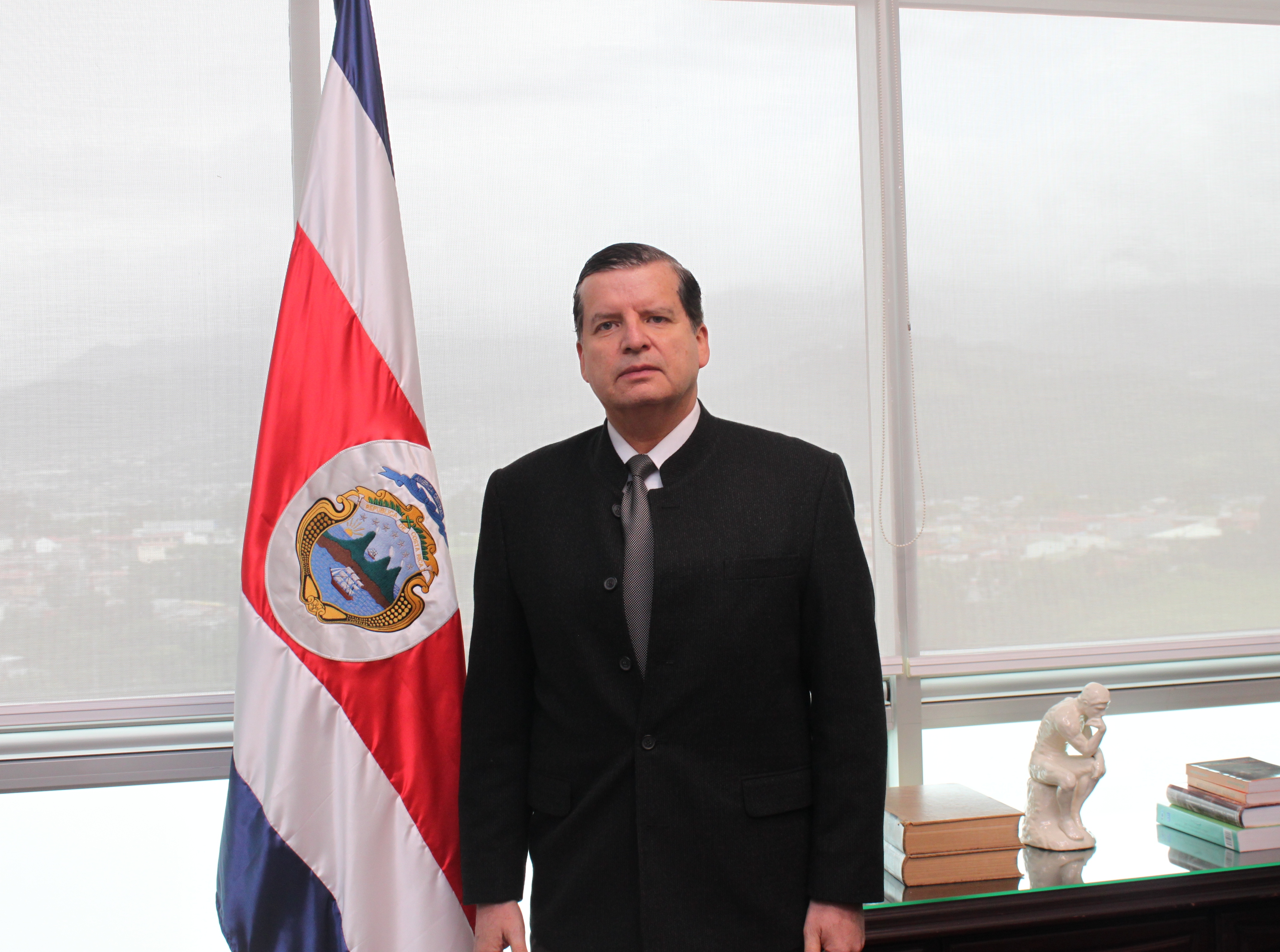 Magistrado Jorge Araya García, de pie, posa para la fotografía junto a la bandera de Costa Rica